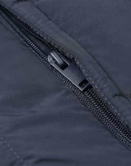 A close-up of a zip on a dark blue insulated puffer vest featuring a branded logo.