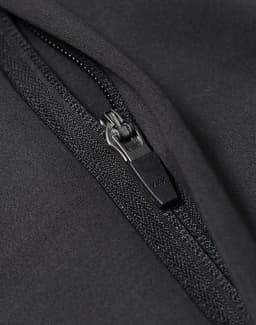 A close-up of a black softshell jacket featuring a zip with a branded pull tab.