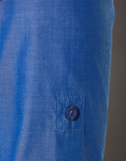 A close-up of a blue women's shirt featuring a button and a rolled-up sleeve. The fabric has a subtle texture.