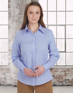 A woman models a blue and white gingham check button-up shirt with long sleeves in a bright indoor setting.