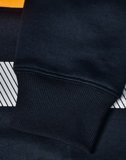 A close-up of a navy blue jumper with a striped design and ribbed cuffs, featuring a logo.