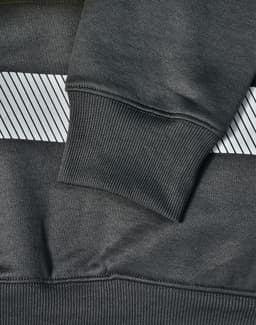A close-up of a dark green jumper featuring a grey striped pattern and ribbed cuffs, with a branding logo.