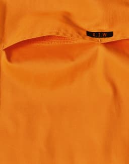 An orange work shirt featuring a pocket and a tag with a logo.