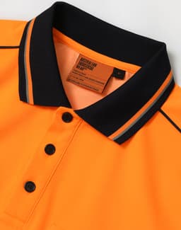 An orange safety polo shirt with black collar and buttons, featuring a tag with care instructions.