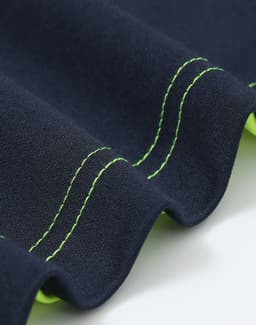 A close-up of a navy polo shirt with bright green stitching and detailing along the edges. It features a logo.