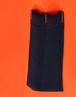 A close-up of a bright orange fleece hoodie featuring a navy blue pocket and contrasting stitching. It has a logo.
