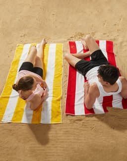 Striped beach towels in yellow and red, laid out on sand, with a man and woman relaxing on them.