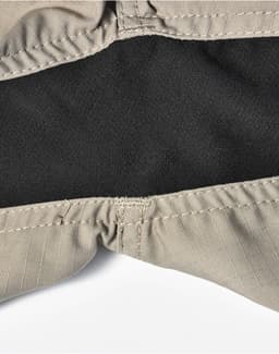 A close-up of beige work shorts featuring a black inner lining and stitched seams, with a logo visible.
