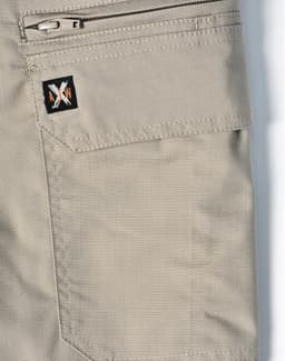 A pair of beige work shorts featuring a zip pocket and a logo patch. The fabric has a rip-stop texture.