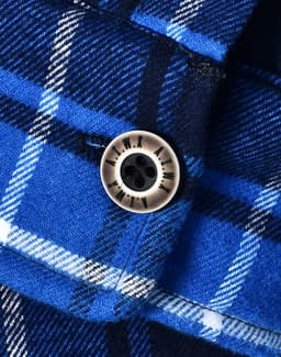 A close-up of a blue and white checkered flannel shirt featuring a round button and a logo.
