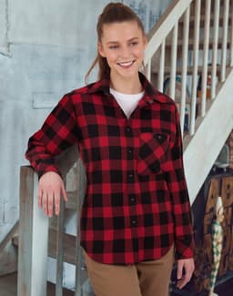 A unisex flannel plaid shirt in red and black, featuring a button-up design and a pocket, worn by a smiling model.