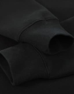 A black crew fleece jumper featuring ribbed cuffs, showcasing a soft fabric texture. It has a branding logo.