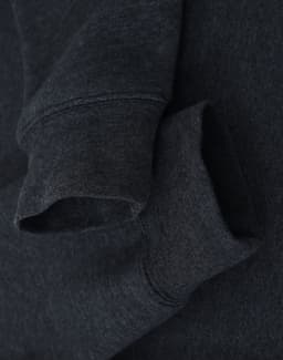 A dark grey crewneck sweatshirt featuring a soft fleece texture and rolled cuffs. It has a logo near the neckline.
