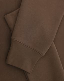 A brown crew fleece jumper with visible cuffs and fabric texture detail. Features a logo.