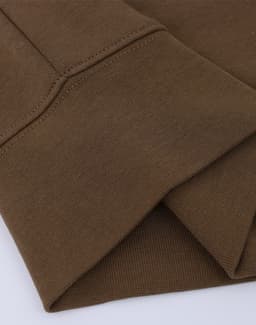 A close-up of a folded brown crew neck sweatshirt featuring ribbed cuffs and a subtle texture. Designed with a logo.