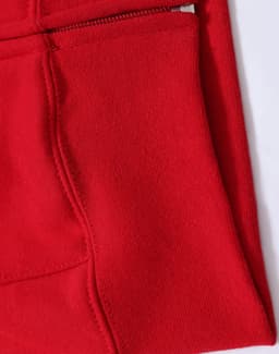A close-up of a red fleecy hoodie featuring a full-zip and zippered pocket. The fabric appears soft and textured.