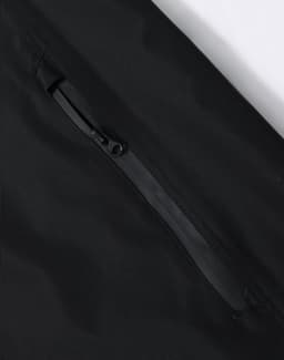 A black waterproof jacket featuring a zippered pocket and a smooth fabric texture. It has a logo on the jacket.