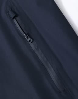 A close-up of a navy waterproof jacket showing a zippered pocket, with a sleek, modern design and a logo.