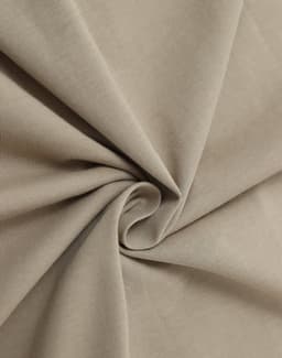 A close-up of soft, beige cotton fabric, showcasing its smooth texture and drape.