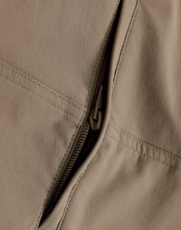 A close-up of beige work pants featuring a zippered pocket, showcasing the fabric and stitching details.
