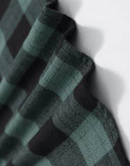 A close-up of a unisex flannel shirt in black and green plaid fabric, featuring a logo.