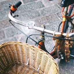 A red bicycle with a wicker basket, featuring a bicycle light attached to the handlebars.