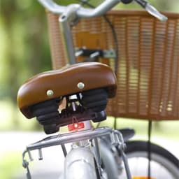 A brown bicycle seat with a red light attached, positioned on a silver bike with a wicker basket.