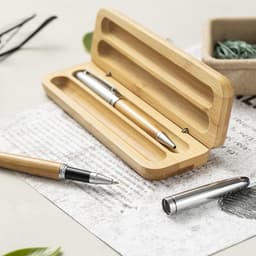 A bamboo pen set displayed in a wooden case with silver accents and a notepad in the background. 