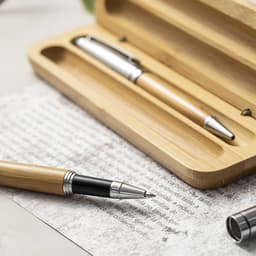 A bamboo pen set in a wooden box, featuring a silver and black pen, placed on textured paper.