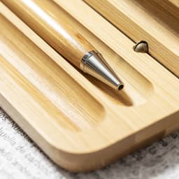 A bamboo pen rests in a wooden holder, featuring a silver tip and a smooth, natural finish.