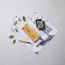 A bamboo pen case with a pen, paper clips, and a small plant pot, accompanied by glasses and a patterned sheet of paper.
