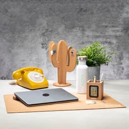 A cork desk mat with a yellow telephone, a plant, a drink bottle, a pencil holder, and a laptop.