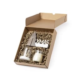 A gift set in a cardboard box, featuring a candle, a glass container, and a wooden Xmas tree, with brown shredded paper.