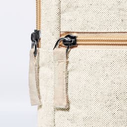 A light beige bag featuring a zipper, with fabric zipper pulls and a textured exterior. It has a logo present.