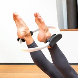 A fitness ring held between feet, featuring a white frame with black grips, used for exercise.