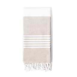 A beige bath towel with white stripes and tassels at the bottom, featuring a logo.