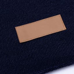 A dark navy scarf featuring a textured knit design and a rectangular leather patch.