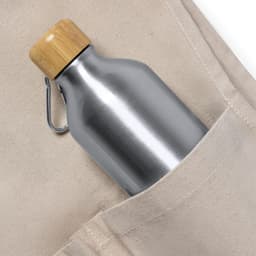 A stainless steel drink bottle with a bamboo lid rests in a beige tote bag pocket.