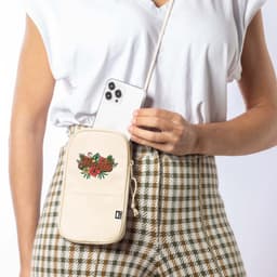 A cream Landry Bag with floral embroidery, held by a person next to a patterned outfit, featuring a mobile phone inside.