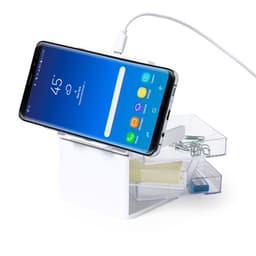 A wireless charger in white with a smartphone propped up, connected by a charging cable, alongside a small storage box.