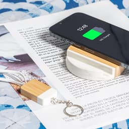 A wireless charger holder in white and bamboo, with a smartphone displaying charging status.