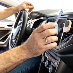 A car phone holder in use, featuring a wooden magnet and a smartphone, set against a blurred car interior.