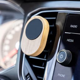 A bamboo car phone holder attached to an air vent, featuring a round black magnetic surface.