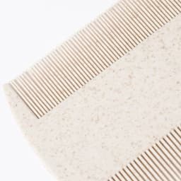 A comb in a cream colour with a textured surface and fine-toothed design. It features an unobtrusive logo.