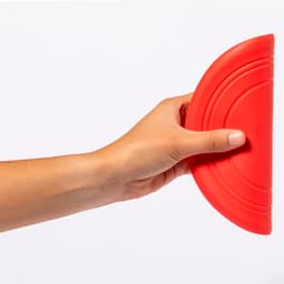 A red frisbee held in a hand, featuring a curved design and a textured grip. It has a logo.