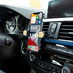 A car phone holder with wooden accents, securely gripping a smartphone mounted in a vehicle's dashboard.