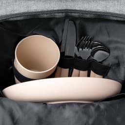 A beige bowl, cup, and cutlery set are neatly arranged inside a grey cooler bag. The bag has a logo.