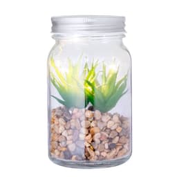 A decorative plant housed in a glass jar with pebbles, featuring green artificial foliage and subtle lighting.