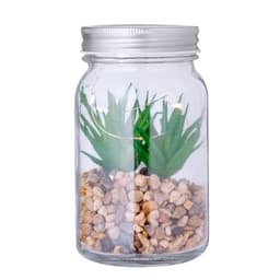 A decorative plant in a clear glass jar, featuring green artificial foliage and a base of small pebbles.