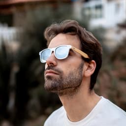 Sunglasses with a wooden frame and grey mirrored lenses worn by a man outdoors.